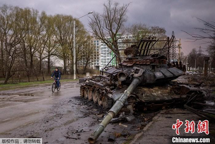 资料图：乌克兰切尔尼夫，一名男子在一辆被毁的坦克旁骑车。