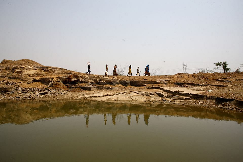 Women and children carry containers after filling them with water at an abandoned stone quarry on a hot day in Chipiya Abhaypur village in the northern state of Uttar Pradesh, India, May 4, 2022. Picture taken May 4, 2022. 