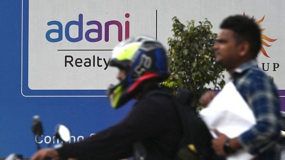 Motorists ride past a signage of an upcoming residential project by Adani Realty, a company under Adani Group
