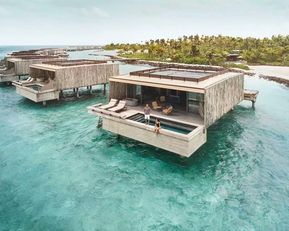 一对夫妇站在或坐在 Patina Maldives Fari 水上平房的游泳池旁