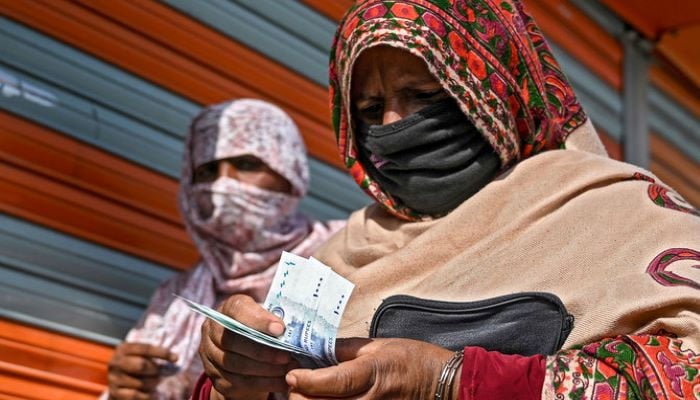 In this file photo, a woman in a face mask counts rupee notes as she walks on a street in Islamabad on April 9, 2020. Photo: AFP