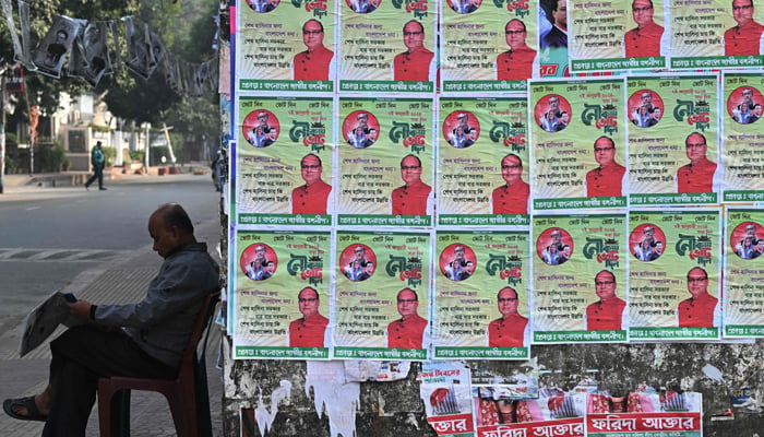 A resident reads a newspaper sitting next to election posters of Awami League party, ahead of the upcoming general elections, in Dhaka on January 5, 2024. — AFP