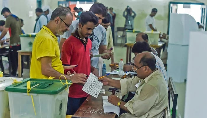 People line up as election officials check their ballot papers during voting in the general election at a polling station in Lahore. — AFP/File