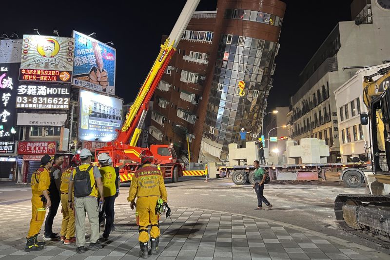 Rescue workers stand near the site of a leaning building in the aftermath of the earthquake.