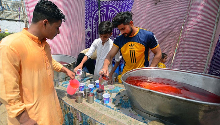 Commuters can be seen quenching their thirst by chilled beverage to beat the heat at a heat stroke relief camp organized by Social Organization, at Shahrah-e-Faisal road in Karachi on June 26, 2024. — APP